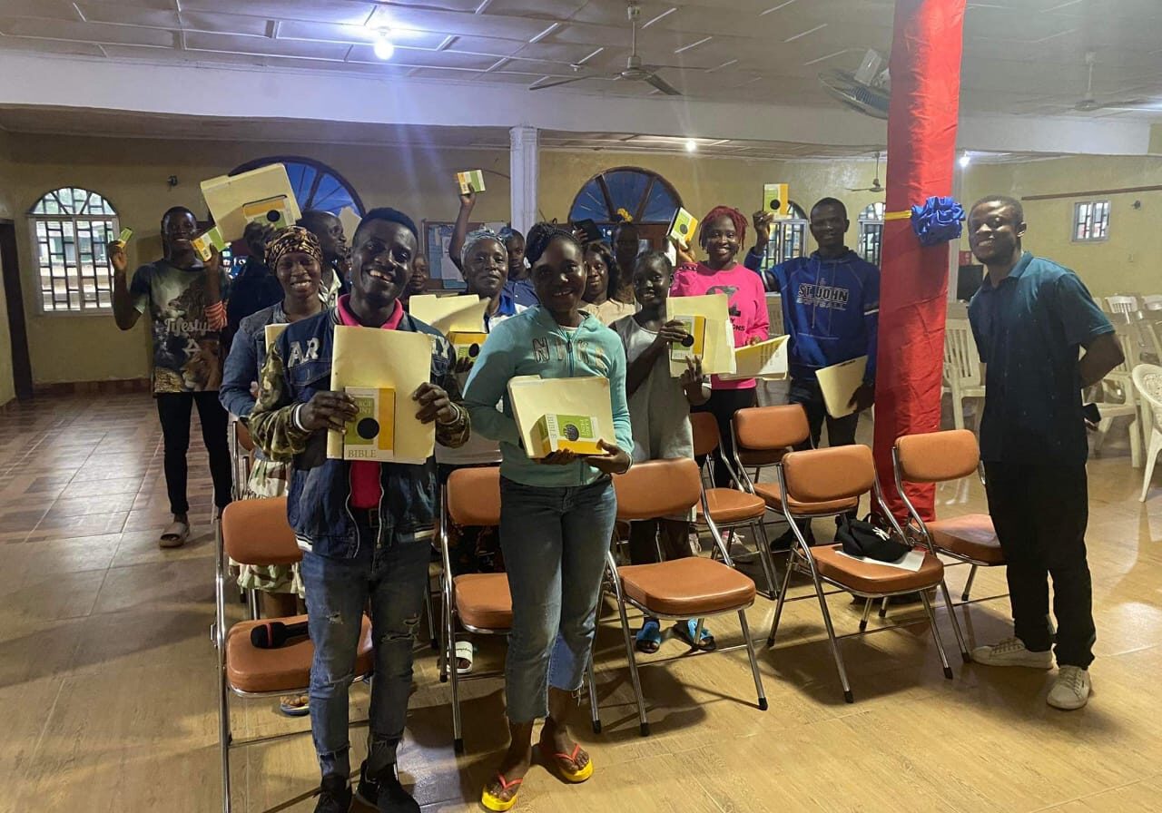 A group of people holding up paintings in front of chairs.